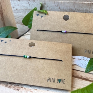 May include: Two friendship bracelets with black string and colourful beads. The bracelets are displayed on brown card stock with the words "With Love" printed on each card.