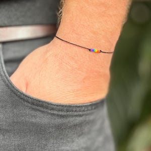 Op de afbeelding: Een zwart koord armband met een regenboog van kleine kralen.