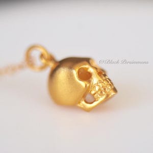 May include: A gold-toned skull pendant necklace. The skull is detailed with eye sockets and teeth.