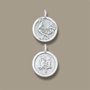Puede incluir: Dos colgantes plateados. El colgante superior presenta un diseño detallado de gallo dentro de un marco circular. El colgante inferior muestra caracteres chinos. Ambos colgantes tienen un lazo para sujetar a una cadena o collar.