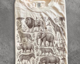 May include: An ivory t-shirt featuring a detailed brown ink illustration of various African wildlife including a lion, giraffe, elephant, rhinoceros, cheetah, leopard, zebra, and hippopotamus, with the word ivory printed in the top right corner.