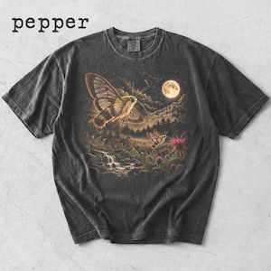 May include: A charcoal gray short-sleeve t-shirt featuring a graphic print of two moths flying over a forest landscape with a waterfall, wildflowers, and a full moon in the night sky. The word pepper is printed in the top left corner of the image.