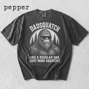 May include: Pepper-colored t-shirt with the text "Dadsquatch" above an illustration of a Bigfoot wearing sunglasses. The text "LIKE A REGULAR DAD, JUST MORE SQUATCHY" is below the illustration. The word "pepper" is in the upper left corner.