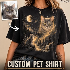 May include: Black t-shirt featuring a custom pet portrait. The design includes a large cat image with yellow eyes, a smaller cat, a moon, and a waterfall. The words "CUSTOM PET SHIRT" are printed at the bottom.