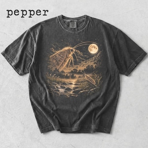 Puede incluir: Una camiseta de manga corta gris carbón con la palabra pepper impresa en la esquina superior izquierda. El centro presenta un gráfico de una polilla grande sobre un paisaje a la luz de la luna con un arroyo, árboles y una polilla más pequeña.