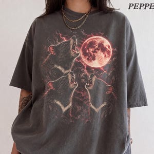 以下が含まれることがあります： チャコールグレーの半袖Tシャツ。赤い稲妻と雲の中で、大きな赤い月に向かって遠吠えする3匹のネズミのグラフィックプリントが施されています。右上に「PEPPER」という文字がプリントされています。クルーネック仕様です。