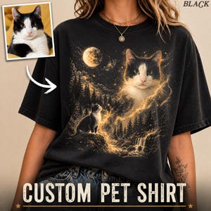 May include: Black t-shirt with a custom pet portrait design. The graphic features a black and white cat with a celestial background, including a moon, stars, and a waterfall. The text "CUSTOM PET SHIRT" is displayed at the bottom.