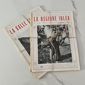 May include: Two vintage Italian magazines, bound with twine. The covers feature text in red and black, with illustrations. One magazine is titled "La Valle E Le Vall" and the other "La Regione Iblea E La Provincia Di Ragusa".