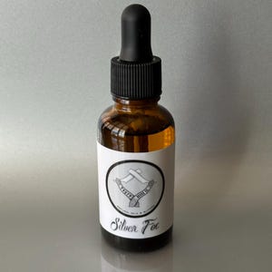 May include: A brown glass bottle with a black dropper top and a white label. The label has a black and white logo with the text "Truth & Ritual" and the words "Silver Fox".