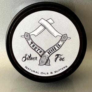 May include: A black and white illustration of two crossed straight razors with the text "Truth Beard Co." and "Silver Fox" on a white background. The text "Natural Oils & Butters" is printed below the razors.