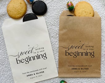 May include: Two paper treat bags, one cream and one brown, with the text "a sweet ending to a new beginning". Each bag contains a biscuit and a chocolate treat. The cream bag has a dark chocolate biscuit.