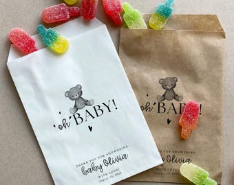 May include: Two white paper bags with brown paper bags inside. The white bags have a teddy bear illustration and the text 'oh' BABY!' printed on them. The brown bags have the text 'oh' BAF!' printed on them. Both bags contain gummy candies shaped like popsicles.