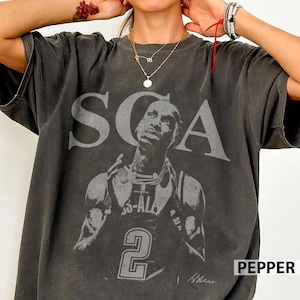May include: A charcoal gray short-sleeve t-shirt featuring a large, faded graphic print of a basketball player wearing a jersey with the number 2. The text SCA is printed in large, distressed capital letters above the player's head.