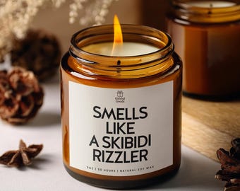 Puede incluir: Una vela encendida en un frasco de vidrio marrón con una etiqueta blanca. La etiqueta dice "Smells Like A Skibidi Rizzler". La vela tiene una mecha encendida y está llena de cera blanca. El frasco es de 255 gramos y tiene un tiempo de combustión de 50 horas.