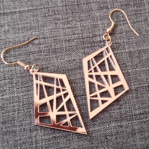 Op de afbeelding: Een paar oorbellen van roségoud met een geometrisch ontwerp. De oorbellen zijn gemaakt van metaal en hebben een diamantvorm met een uitgesneden patroon.