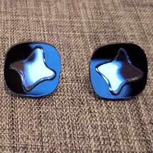 May include: A pair of blue and silver star-shaped earrings. The earrings are square-shaped and have a star-shaped design in the center.