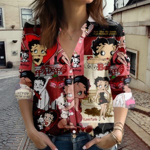 May include: A patterned button-down shirt with a collage of Betty Boop illustrations in red, pink, and cream. The design includes hearts, cherries, and the text "I Love Paris" and "Just like the moon, I go through phases."