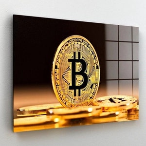 May include: A gold-colored Bitcoin coin with the text "Bitcoin Decentralized Peer-to-Peer Digital Currency" around the edge. The coin is sitting on top of a stack of other gold-colored coins.