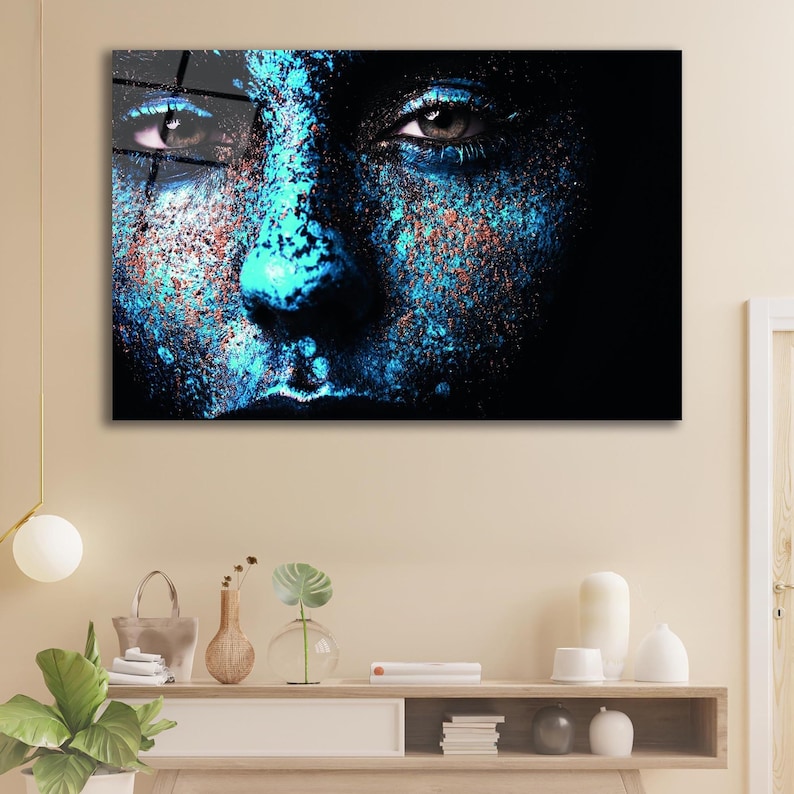 May include: Close-up of a person's face with blue and orange paint splatter. The person's eyes are looking directly at the viewer.