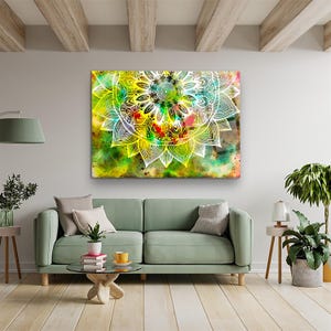 Puede incluir: Una gran obra de arte en lienzo rectangular con un diseño de mandala blanco sobre un fondo abstracto colorido. El fondo mezcla tonos verdes, amarillos, rojos y marrones. La obra de arte cuelga sobre un sofá verde en un salón.