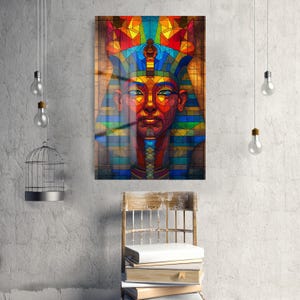 May include: A vibrant stained-glass style artwork of an Egyptian pharaoh's bust. The artwork uses a rich palette of blues, reds, yellows, and greens, with detailed geometric patterns. The artwork is displayed on a wall, with a wooden chair and books in front.