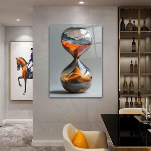 May include: A glass hourglass with orange and gray sand inside. The hourglass is on a white background.