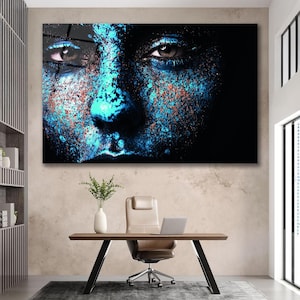 May include: A close-up of a person's face with blue and orange paint splattered on it. The person's eyes are looking directly at the viewer.