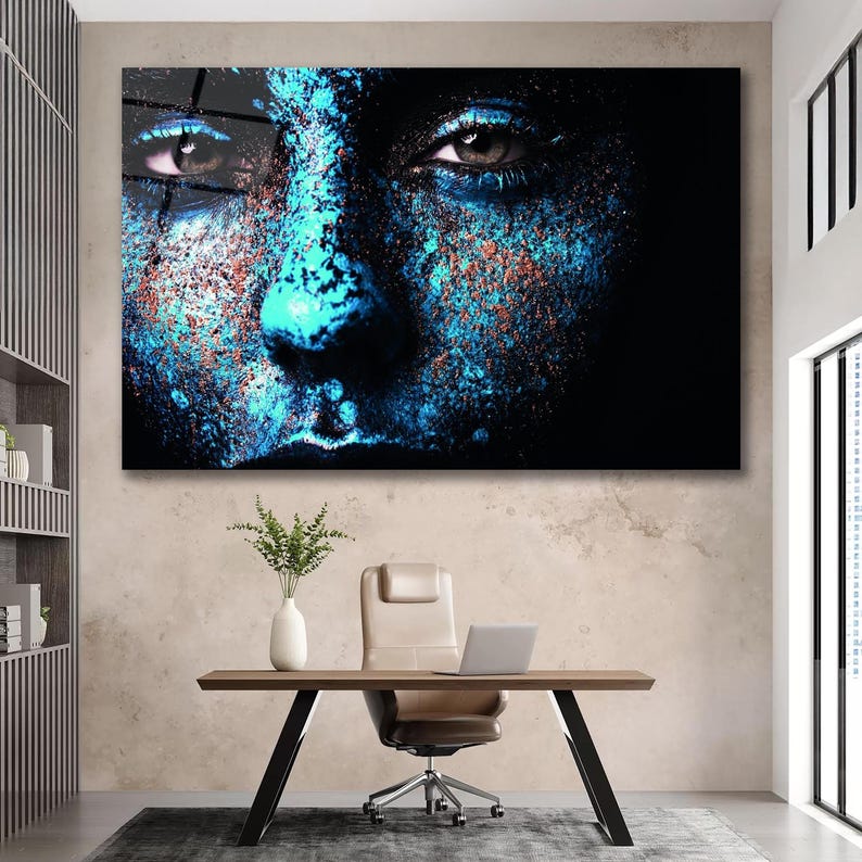 May include: A close-up of a person's face with blue and orange paint splattered on it. The person's eyes are looking directly at the viewer.