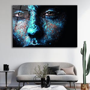 May include: Close-up of a person's face with blue and orange paint splatter. The person's eyes are closed and their mouth is slightly open.