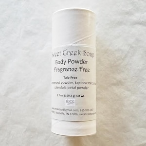 Peut inclure: Tube blanc de poudre pour le corps Sweet Creek Soap, étiqueté "Fragrance Free" et "Talc-Free". Les ingrédients sont indiqués comme "poudre de racine de flèche, amidon de tapioca, poudre de pétale de calendula". Le tube indique également le poids net comme étant "3,7 oz (109,2 g)".