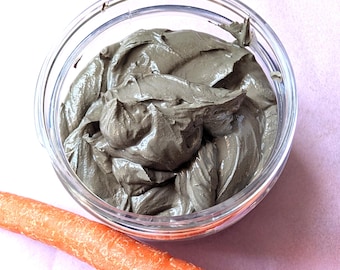May include: A clear glass jar filled with a gray, smooth, and creamy substance. A bright orange carrot is lying on a pink surface next to the jar.
