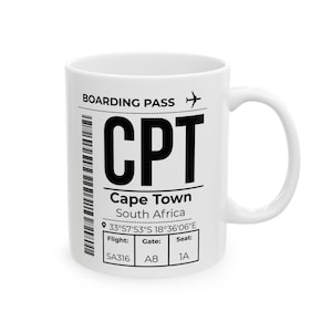 May include: A white ceramic mug featuring a black printed graphic of a boarding pass for Cape Town, South Africa. The design includes the airport code CPT, coordinates 33°57'53"S 18°36'06"E, flight SA316, gate A8, and seat 1A with a barcode and aeroplane icon.
