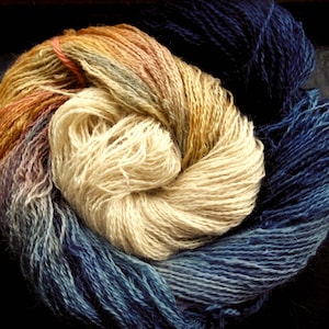 May include: A close-up of a skein of yarn in shades of cream, orange, brown, and blue. The yarn is tightly wound, with the colours blending together. The yarn is likely used for knitting or crocheting.