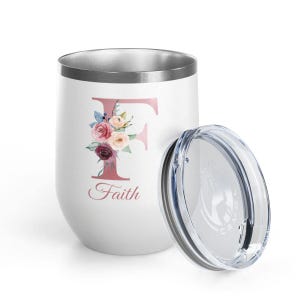 Può includere: Bicchiere da vino isolato bianco con un design floreale "F" e la parola "Faith" in corsivo. Il bicchiere ha un bordo argentato e viene fornito con un coperchio trasparente. Il design presenta fiori rosa, bordeaux e crema.