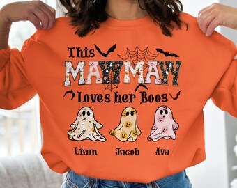 May include: Orange sweatshirt with the text "This Mawmaw Loves her Boos" and three ghost illustrations. The names Liam, Jacob, and Ava are printed below the ghosts. Bats and spiderwebs are also featured.