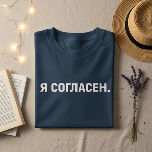 May include: A dark blue t-shirt featuring the white text "Я СОГЛАСЕН." printed in a clean, sans-serif font across the center of the chest. The garment has a classic crew neckline and short sleeves, presented in a flat, folded orientation.