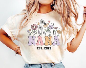 May include: Cream-coloured t-shirt featuring a floral design and the word "NANA" in pastel shades. The design includes flowers, butterflies, and the text "EST. 2025".