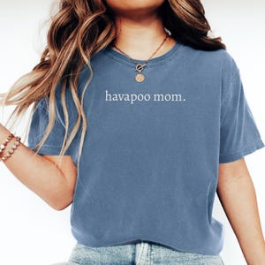 May include: A dusty blue t-shirt with the text "havapoo mom." in white. The shirt has short sleeves and a crew neck. The shirt is made of a soft material.