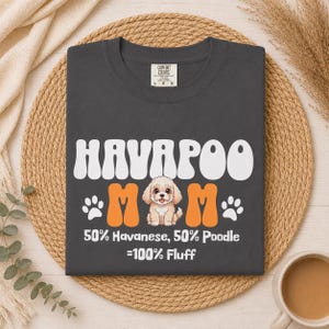 May include: Dark gray Comfort Colors t-shirt with the text "HAVAPOO MOM" in white and orange. The shirt features a cartoon image of a Havapoo dog and the text "50% Havanese, 50% Poodle = 100% Fluff."