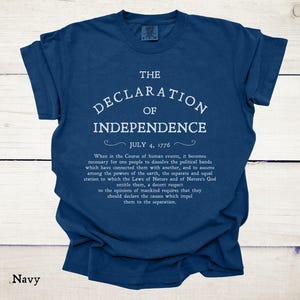 May include: Navy blue t-shirt featuring the text "THE DECLARATION OF INDEPENDENCE" in white, along with the date "JULY 4, 1776" and a quote. The shirt is a comfortable, casual wear item.