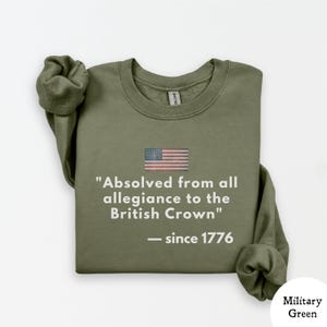 May include: Military green sweatshirt with the American flag and the text "Absolved from all allegiance to the British Crown" and "since 1776". The sweatshirt has a crew neck and long sleeves.