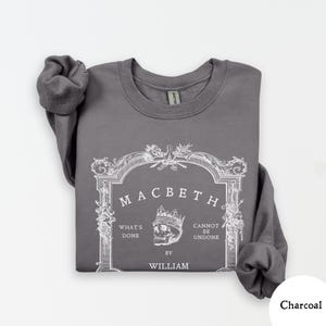 May include: Charcoal gray sweatshirt featuring a white graphic from Shakespeare's Macbeth. The design includes the title, a skull wearing a crown, and the phrases "What's Done" and "Cannot Be Undone" with "By William" below.