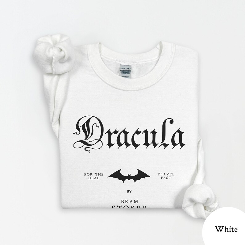 Op de afbeelding: Witte sweatshirt met het woord "Dracula" in gotisch lettertype. Daaronder een vleermuisafbeelding en de zinnen "For the Dead" en "Travel Fast". De naam van de auteur, Bram Stoker, staat ook op de trui.