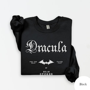 Op de afbeelding: Zwarte sweatshirt met het woord "Dracula" in een gotisch lettertype. Daaronder een vleermuisafbeelding en de tekst "For the Dead", "Travel Fast" en "By Bram Stoker".