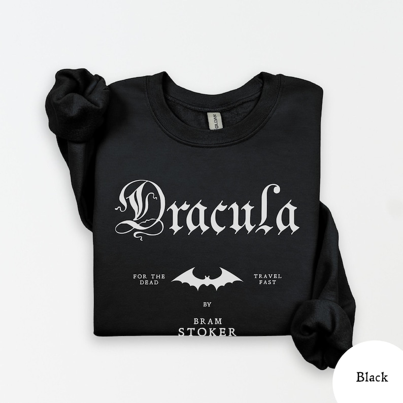 Op de afbeelding: Zwarte sweatshirt met het woord "Dracula" in een gotisch lettertype. Daaronder een vleermuisafbeelding en de tekst "For the Dead", "Travel Fast" en "By Bram Stoker".