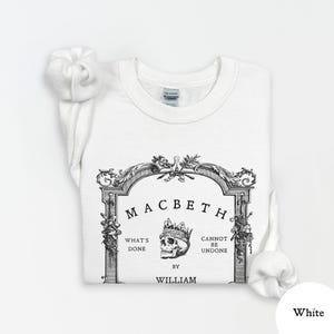 May include: White sweatshirt featuring a black and white graphic design. The design includes the word "Macbeth" above a skull wearing a crown, with text that reads "What's Done Cannot Be Undone" and "By William."
