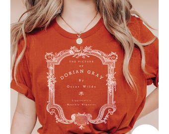 May include: Rust-colored t-shirt featuring the title of Oscar Wilde's novel, "The Picture of Dorian Gray," in a decorative frame. The text includes the author's name and the magazine title. The shirt has short sleeves and a round neckline.