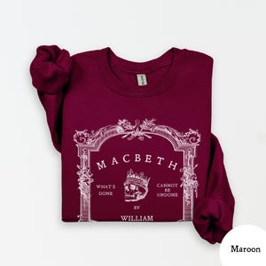 May include: Maroon sweatshirt with the word "Macbeth" in a decorative frame. The design includes a skull wearing a crown and the phrases "What's Done" and "Cannot Be Undone" with the author's name, William.