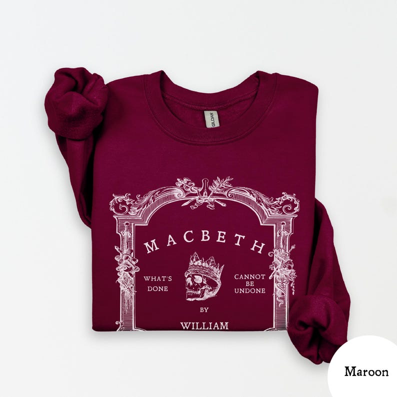 May include: Maroon sweatshirt with the word "Macbeth" in a decorative frame. The design includes a skull wearing a crown and the phrases "What's Done" and "Cannot Be Undone" with the author's name, William.