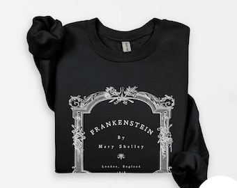 May include: Black sweatshirt featuring a white graphic of a vintage book cover. The graphic reads "FRANKENSTEIN" by Mary Shelley, with "London, England" at the bottom. The sweatshirt is made of a soft material.